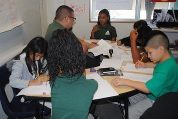 A teacher working with students on writing at a collaborative table