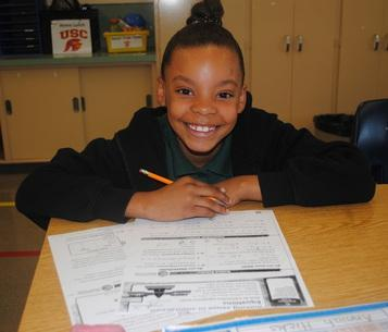 A student smiling while working at her desk in a classroom