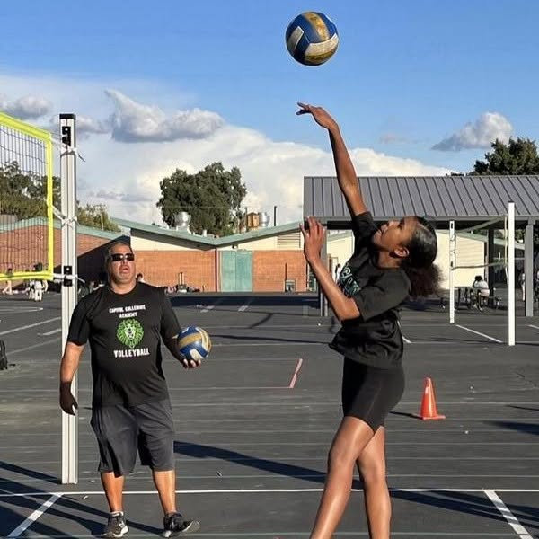 A student practicing volleyball with a coach on an outdoor court
